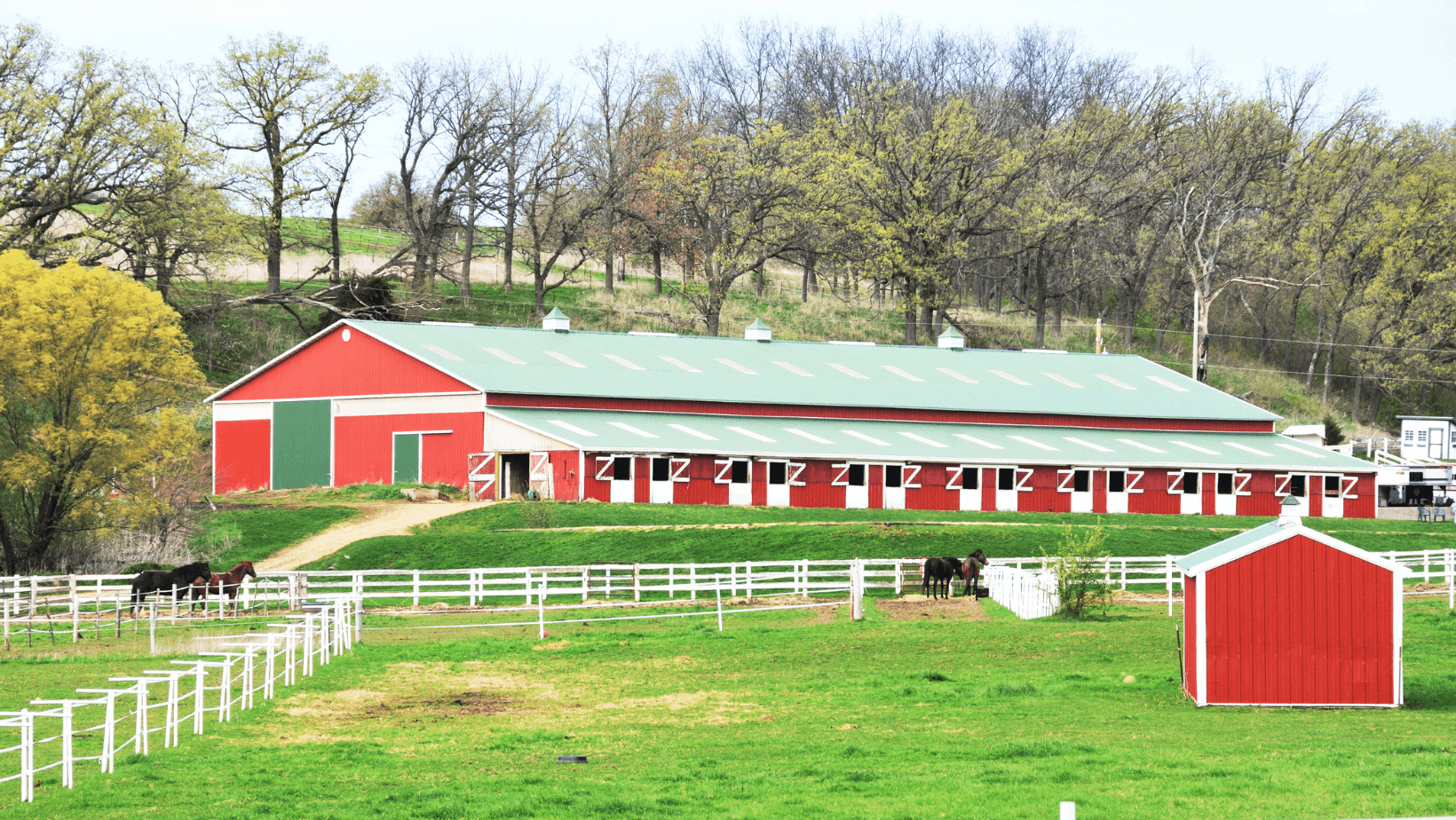 Large Fenced Horse Barn Alt Text: Huge fenced horse barn on lush fields.