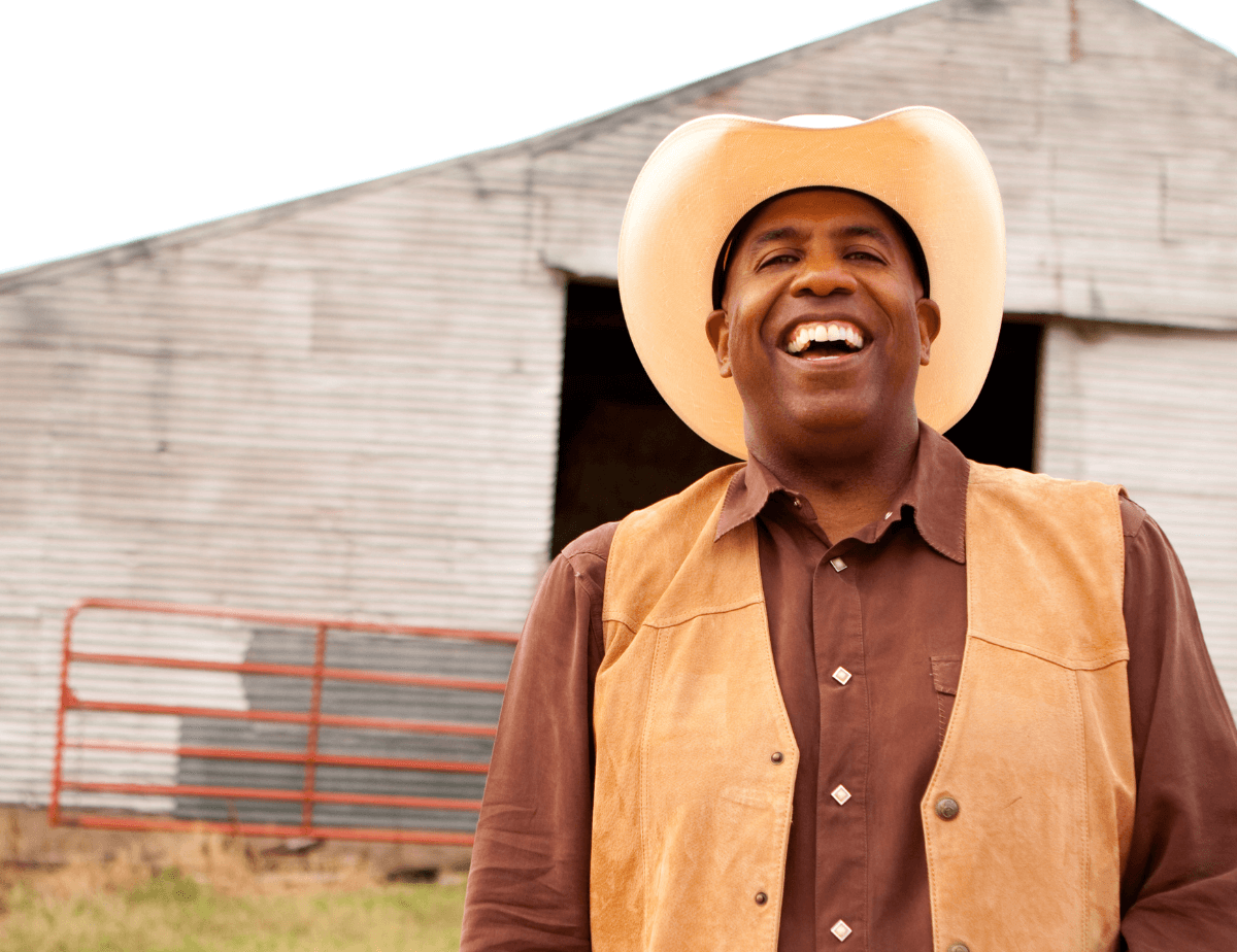 Contented black male farmer with huge barn in the background.