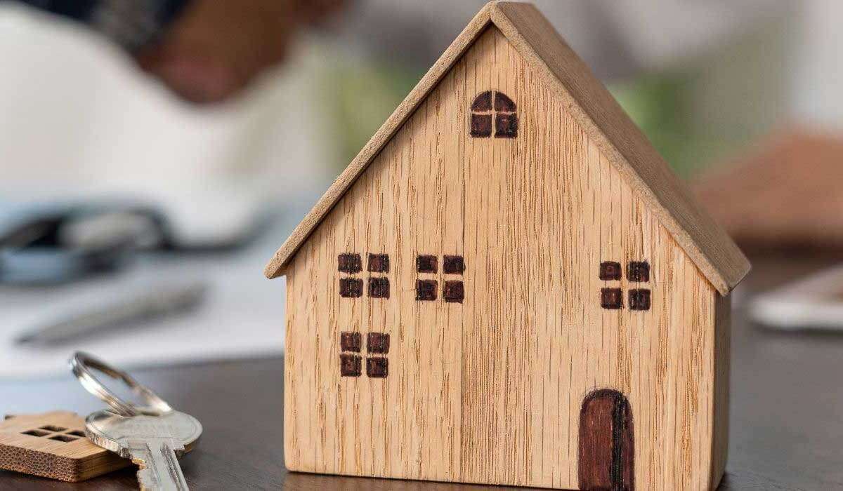 A handshake between two people with a wooden house model and keys on a table, symbolizing the completion of a farm sale transaction in Alberta.