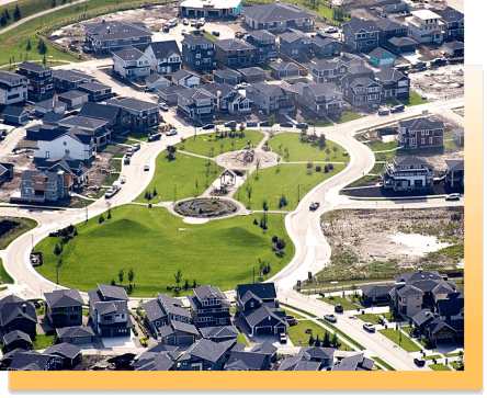 Aerial view of a modern suburban neighborhood featuring a central green park with walking paths and playground, surrounded by newly constructed homes.