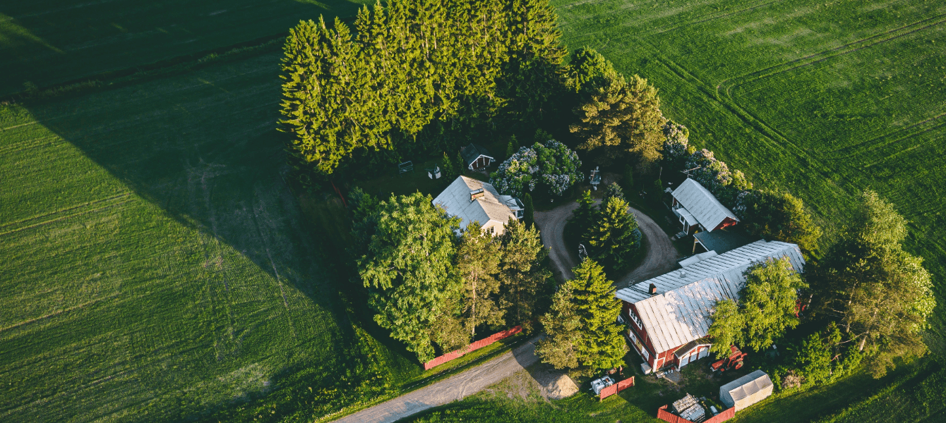 Serene aerial view showcasing expansive farmland featuring a classic red barn, scattered houses, and lush fields.